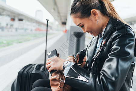 坐在火车平台上的女人拿着手机翻手提包图片