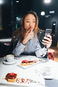 坐在餐厅吃甜点使用智能手机的妇女图片