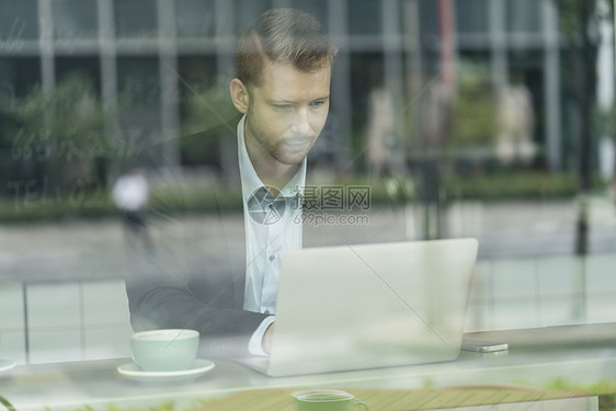 通过窗口看到坐在咖啡馆的商人使用笔记本电脑图片