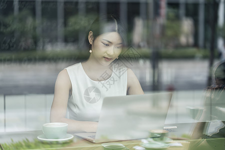 通过窗口看到坐在咖啡馆的女商人使用笔记本电脑图片