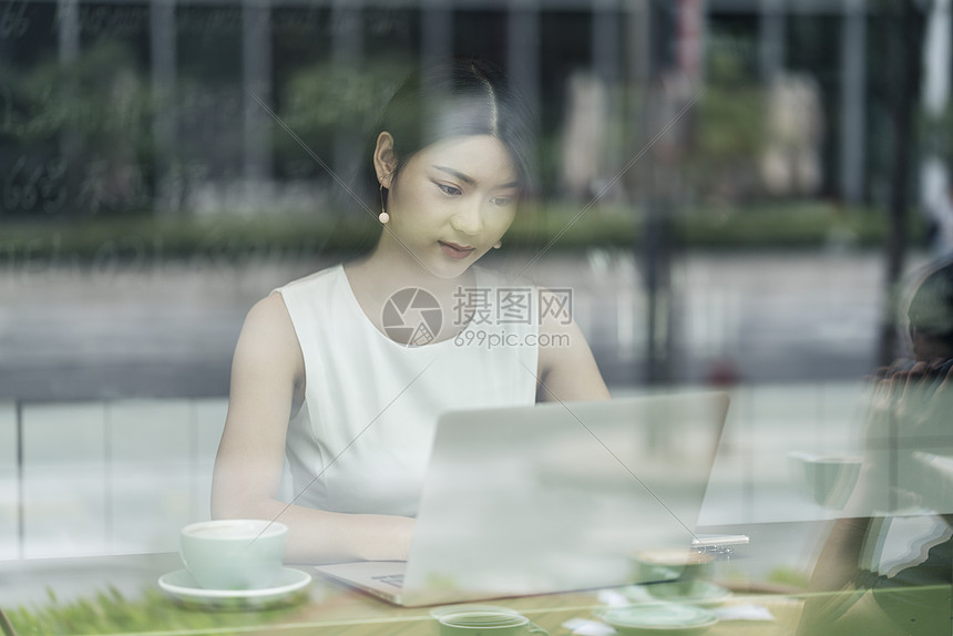 通过窗口看到坐在咖啡馆的女商人使用笔记本电脑图片