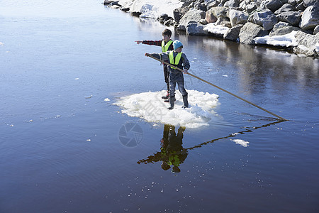 两个男孩站在湖上的冰块上用杆子划动图片