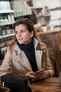 坐在咖啡厅桌边的年轻女子手持智能手机图片