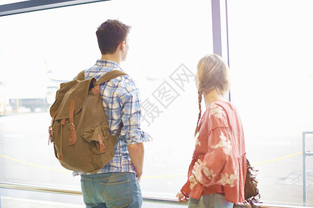 机场的年轻夫妇背着包向窗外看图片