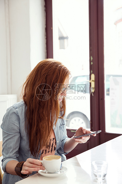 在咖啡馆使用移动电话的年轻妇女图片