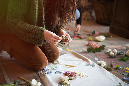 妇女跪在地板上在纺织布上摆放花头背景图片