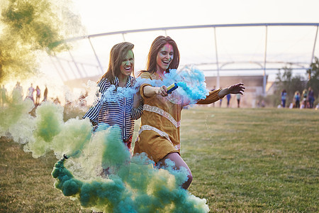 在音乐节拿着彩色烟雾弹跳舞的两名年轻妇女图片