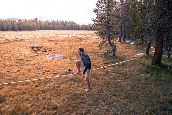 美国加利福尼亚州约塞米蒂公园草甸上一名年轻人在松弛线上练习平衡图片