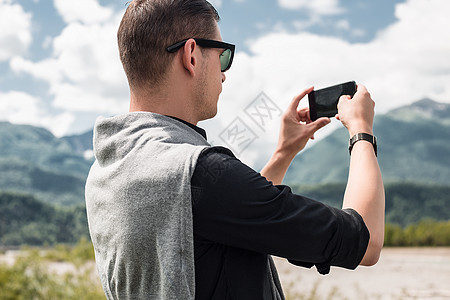 在意大利维内托山河边用手机拍照片的男游客图片