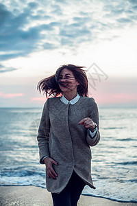 年轻女子的肖像站在沙滩上她回到海洋风吹她的头发微笑图片