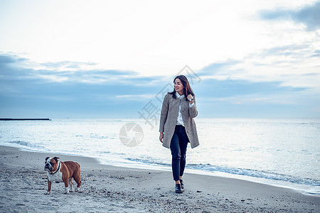 年轻女子带着宠物狗在海滩上散步图片