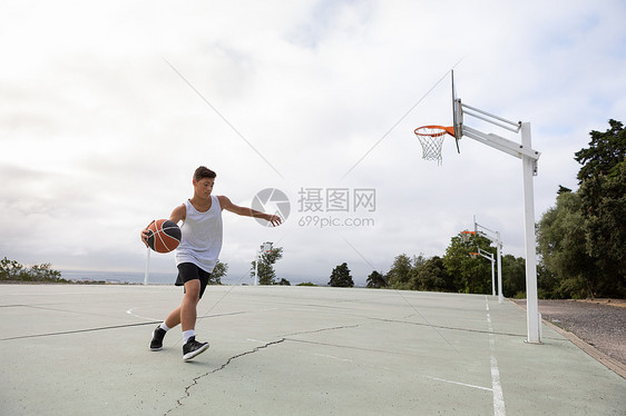 少年男子篮球运动员在篮球场上带球奔跑图片