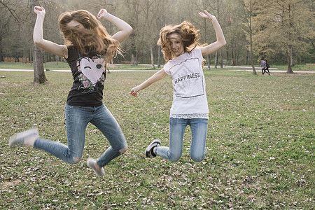 快乐的女朋友们在公园中跳跃欢乐图片