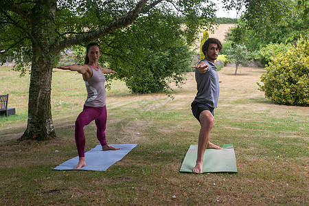 男人和女人在花园做瑜伽练习武士姿势图片