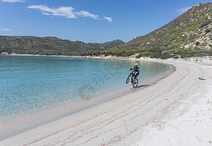 运动性意大利撒丁岛比亚西米乌斯海滩上骑车的人背景