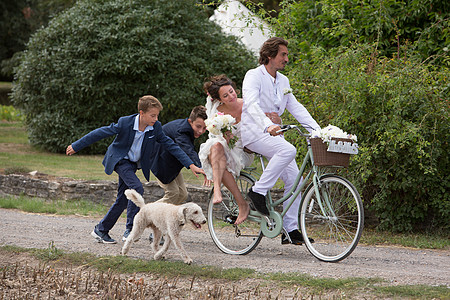 年轻的婚礼客人追赶骑自行车的新婚夫妇图片