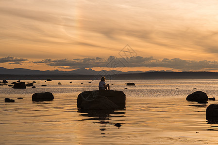 加拿大坎贝尔河日落时坐在岩石上的年轻妇女图片