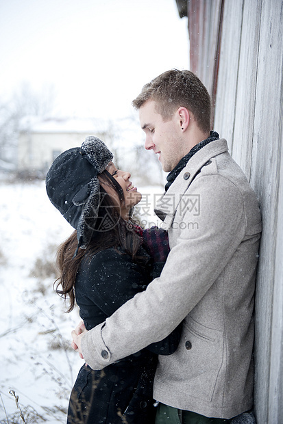 年轻夫妇在雪中拥抱小屋图片
