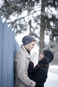 在雪中拥抱栅栏的年轻夫妇图片