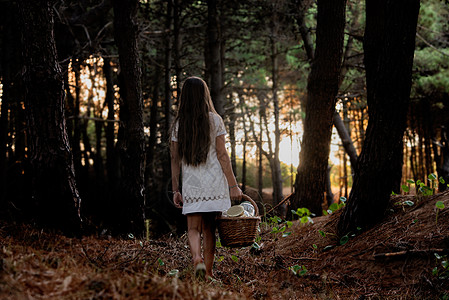 女孩背着野餐篮子走过黑暗森林后视图片