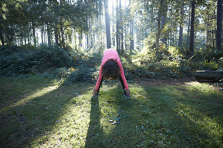 年轻女向前弯曲在森林中伸展图片