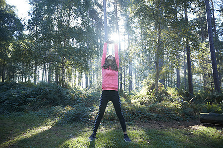 女跑者伸展手臂在日光森林升温图片