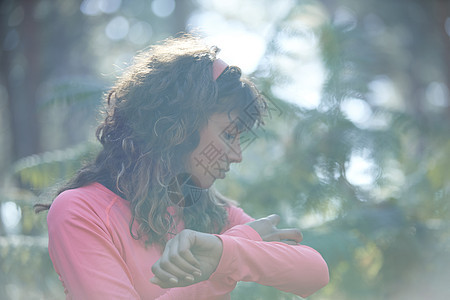 年轻女跑者在日光林中佩戴臂带图片