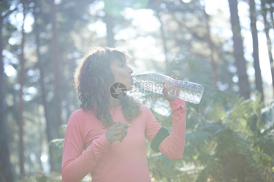年轻的女慢跑者在日光林饮用瓶装水图片