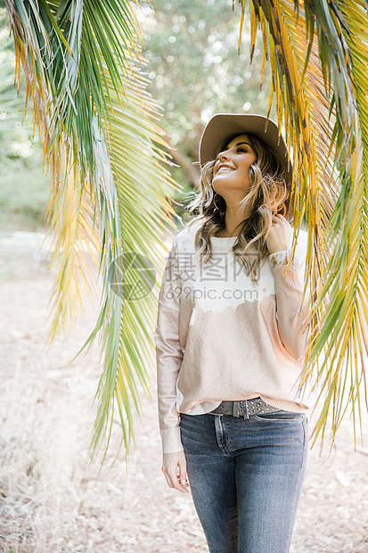 女人站在棕榈叶边抬着头微笑图片