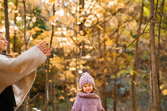 母亲和女儿在森林中把秋叶撒在空中图片
