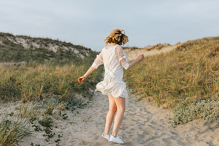 海滨沙丘上穿着白色连衣裙开心跳舞的年轻女子图片