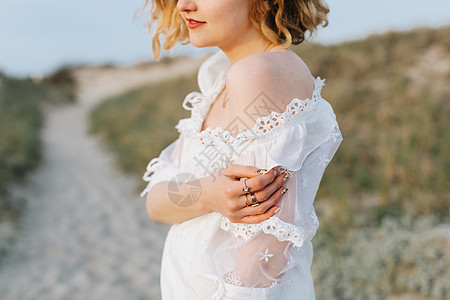 海滨沙丘上穿着白色连衣裙的年轻女子露肩膀图片