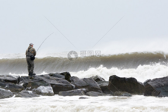 美国纽约长滩在暴风雨的海浪中从岩石上钓鱼的人图片