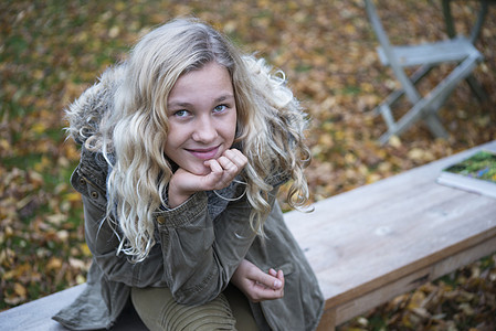 秋天坐在花园长椅上的金发女孩对镜微笑图片