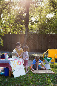 男孩和两个年轻的姐妹在花园里准备柠檬水摊位图片