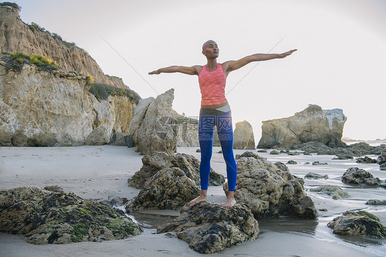 年轻女人站在海滩的岩石上手臂伸展图片
