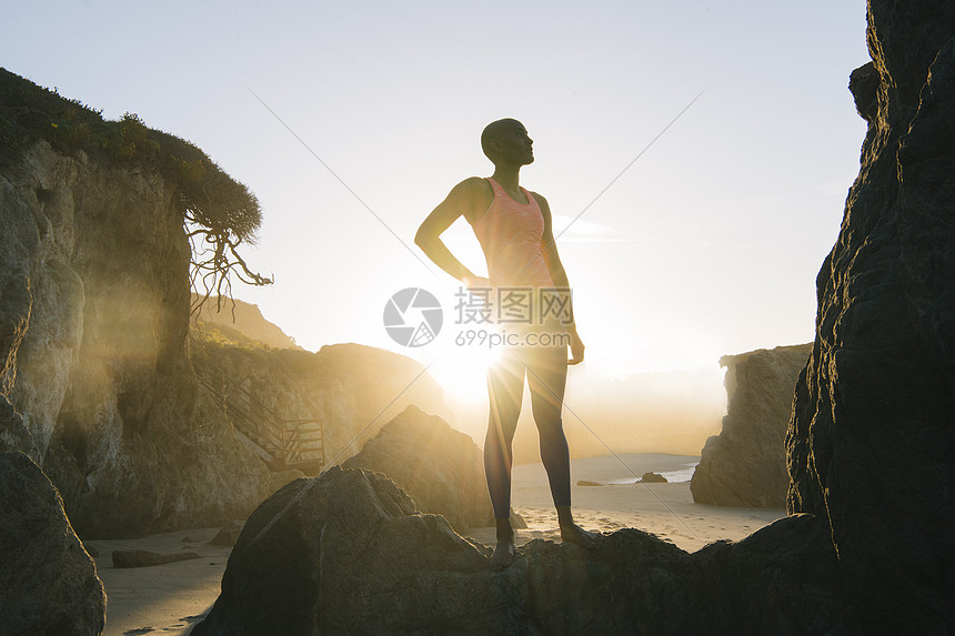 年轻女人站在海滩的岩石上看着风景图片