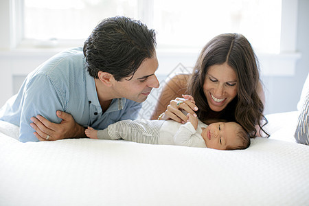 母亲和父亲靠在床上看着新生的男婴儿图片