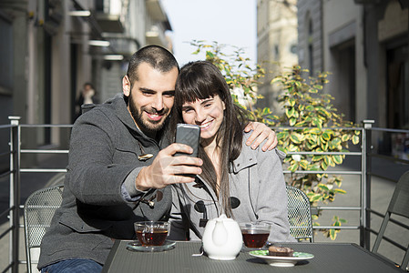 坐在咖啡馆外面的年轻夫妇用手机自拍图片