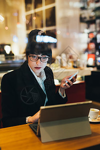在咖啡馆使用移动电话和平板电脑的女商人图片