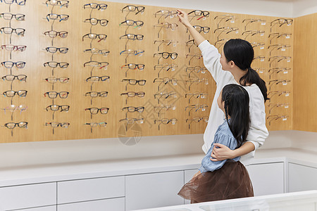 眼镜店里妈妈帮女儿挑选眼镜背景图片