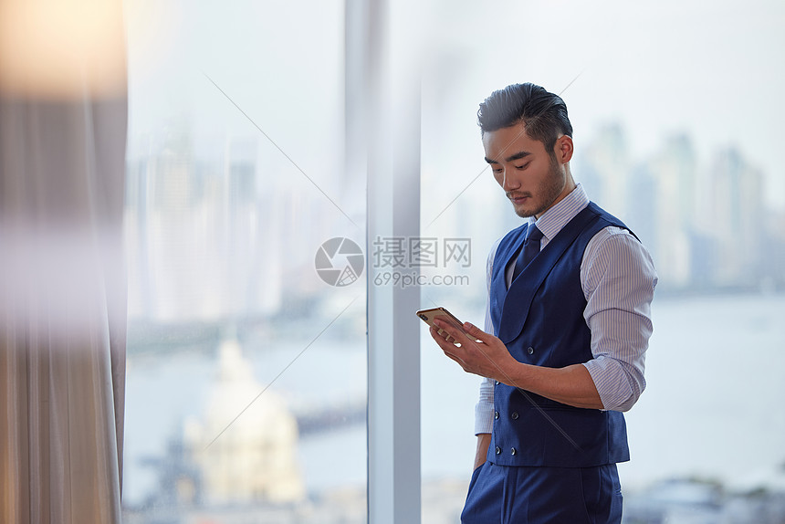 成熟商务人士站在窗前低头看手机图片