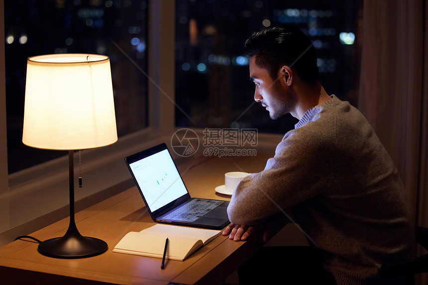 坐在书桌前熬夜加班的男性图片