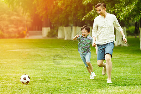 家庭保护快乐父子在草地上踢足球背景