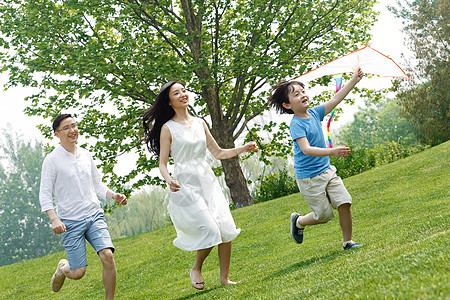 跑可爱学龄前儿童相伴一家三口在草地上放风筝背景