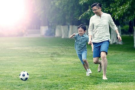 单亲家庭快乐父子在草地上踢足球图片