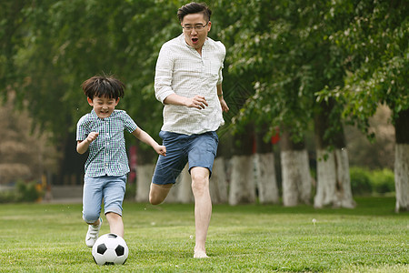 30多岁独生子家庭保护快乐父子在草地上踢足球图片