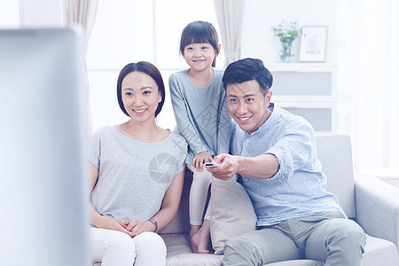 摄影三个人独生子家庭幸福的一家三口在客厅看电视图片