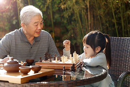 智慧休闲60多岁祖父和孙女在庭院里下棋图片