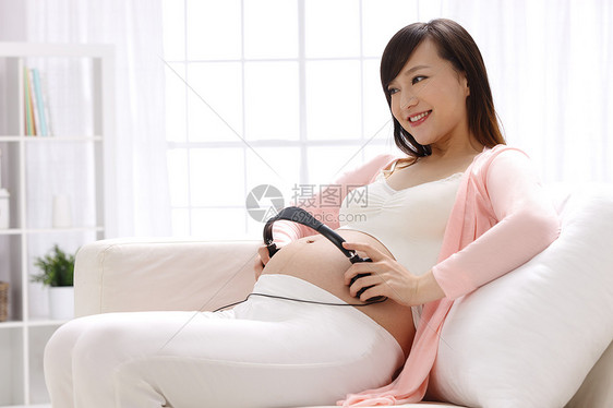 健康的20多岁坐着孕妇把耳机放在肚子上图片